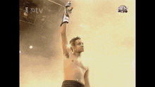 a shirtless man holds his arm up in the air in front of a tv screen that says live