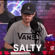 a man wearing a vans shirt and a hat is sitting in front of a microphone