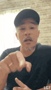 a man with a beard wearing a black hat is pointing at the camera .