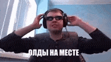 a man wearing headphones and sunglasses is sitting in front of a window with his hands on his ears .