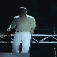 a man in a green shirt and white pants is standing on a stage in front of a microphone .