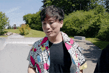 a man wearing a colorful shirt is standing in front of a skate park