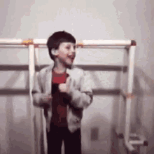 a young boy in a red shirt is standing in front of a ladder and smiling .