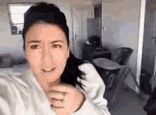 a woman is taking a selfie in a living room while wearing a white robe .