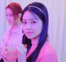 a woman in a pink shirt is eating a lollipop with a straw while another woman looks on .