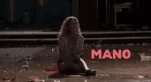 a woman is sitting on the ground in front of the word mano .