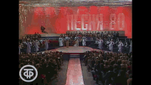a group of people are dancing on a stage with the number 80 in white letters behind them