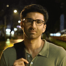 a man wearing glasses and a green polo shirt looks at the camera