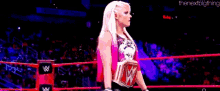 a woman in a pink tank top is standing in a wrestling ring holding a wrestling belt .