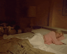 a woman in a pink sweater is sleeping on a bed in a dark room
