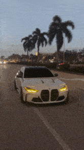 a white bmw is driving down a city street with palm trees in the background