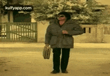 a man is walking down the street holding a briefcase and a cigarette .
