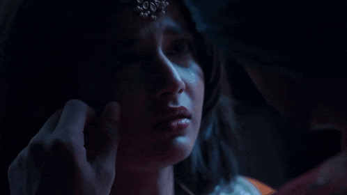 a man wearing a turban looks at a woman in a dark room