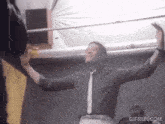 a man in a black shirt and tie is dancing with his arms outstretched and the website gifrun.com is below him