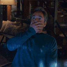 a man in a blue sweater is standing in a dark room with his hands up .