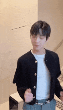 a young man wearing a black cardigan and a white shirt is standing in a room .