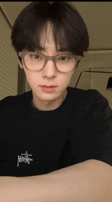 a young man wearing glasses and a black shirt that says stussy on it