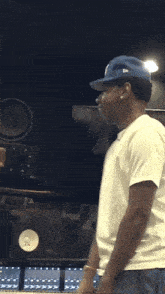 a man wearing a white shirt and a blue hat is standing in front of a speaker