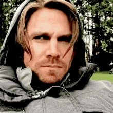 a man with long hair and a beard wearing a grey jacket with a hood