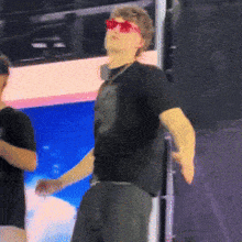 a man wearing sunglasses and a black shirt is standing in front of a sign