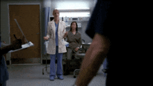 a woman in a lab coat is standing in a hospital room with other people