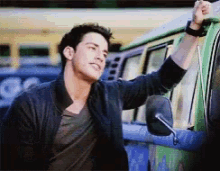 a man in a black jacket is leaning against a blue van
