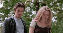 a man and a woman are standing next to each other in front of trees