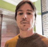 a man with a beard wearing a yellow sweater looks at the camera
