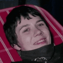 a young man with a bandana around his neck is smiling while laying in a chair .