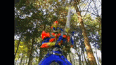 a man in a blue and orange costume is holding a sword in the woods .