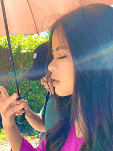 a woman holding a pink umbrella with a man in a black hat standing behind her