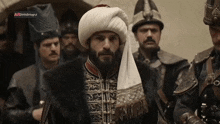 a man with a beard wearing a turban is standing in front of a group of men .