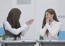two girls are sitting at desks with their hands on their face