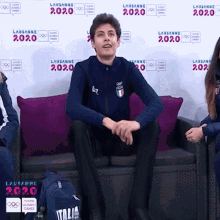 a man sits on a couch in front of a wall that says 2020
