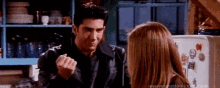 a man and a woman are standing next to each other in a kitchen and the man is making a fist .