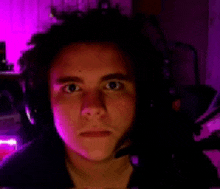 a man wearing headphones looks at the camera with a purple background