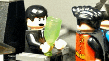 a man in a suit is holding a green glass while a man in a red cape is holding a bottle