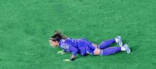 a female soccer goalie is crawling on the grass on her knees .
