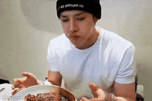 a man in a white shirt and black hat is eating a steak .