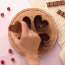 a person is making chocolate hearts on a wooden board