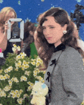 a woman is standing in front of a bunch of flowers and a camera