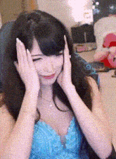 a woman in a blue dress is covering her face with her hands while sitting in a chair .