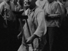 a black and white photo of a man with a cane dancing in a crowd of people .