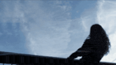a silhouette of a woman standing on a balcony with a blue sky in the background