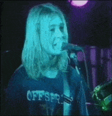 a man with long hair is singing into a microphone while wearing a blue shirt .