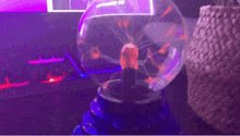 a plasma ball is sitting on a table with a purple light behind it .