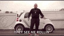 a man is standing in front of a white car and says they see me rollin '
