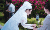 a bride in a white dress and veil stands next to a woman holding flowers