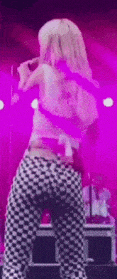 a woman is dancing on a stage with a microphone in her hand while wearing checkered pants .