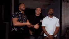 three men are standing next to each other in a dark room and one of them is pointing at something .